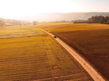 A car on a country lane, surrounded by wide, autumnal fields in soft light, electric car VW ID5,