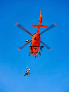 Mountain rescuer of the Bavarian Mountain Rescue Service being winched by the on-board mechanic of