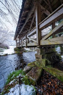 Detailed view of a wooden bridge over a stream with snow and stone substructure, Kälberbrücke,