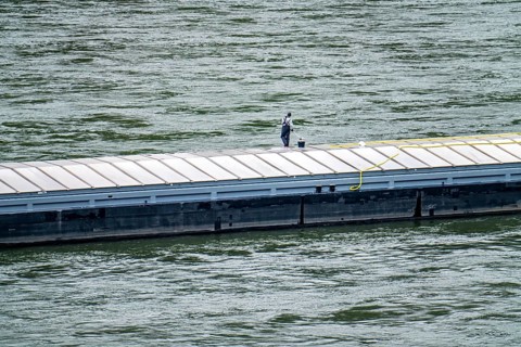 Inland waterway vessel, freighter, with closed cargo hatches, employee cleans the deck with water