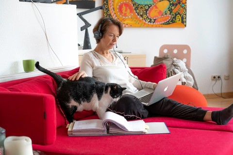 Woman, mid-50s, works from home, with laptop and communicates with colleagues via headset, home