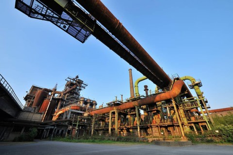 Abandoned industrial site with rusty pipes and dilapidated factory buildings under a clear blue