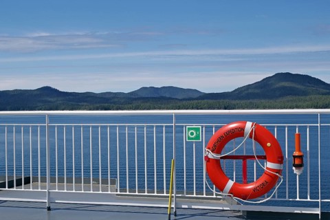 View of the sea from a ship with a lifebuoy and mountains in the background under a clear sky, BC
