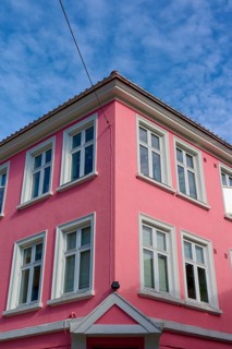 Historic building with pink facade and white window frames under a blue sky with light clouds,