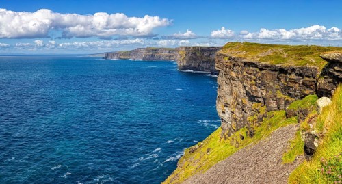 Sunlit cliffs on an endless blue coastline under a clear sky, Cliffs of Moher