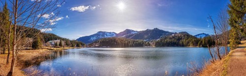 Large mountain lake with calm water surface, sunshine and picturesque mountain landscape,