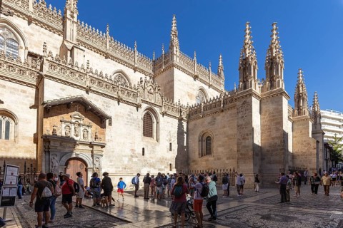 Gothic cathedral with elaborate decorations and tourists in the sunny inner courtyard, Granada