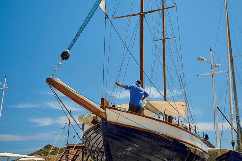 A man repairs the wooden sailing boat at the mast under a blue sky, Patmos Marine, boatyard,