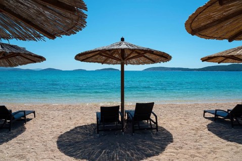 Sunny beach with deckchairs under straw umbrellas. Turquoise sea with islands in the background,