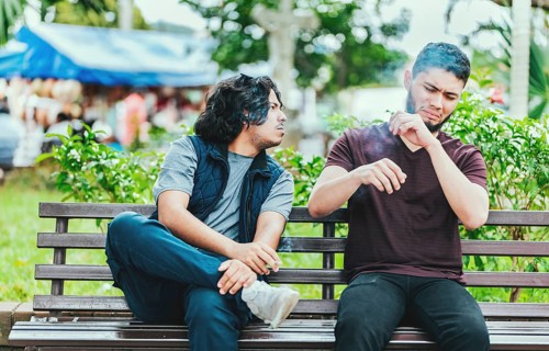 Man smoking and exhaling smoke to another person near him. Man smoking cigarette near people in
