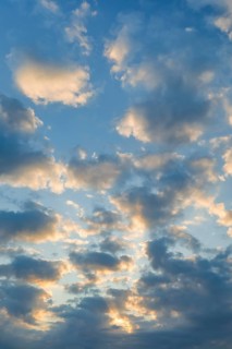 Sun breaks through cloud cover and illuminates fleecy clouds in the evening blue sky