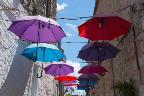 Colourful umbrellas hanging between old buildings under a clear blue sky, Old Town, Areopoli,