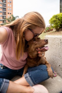 A affectionate woman hugs her pet, gives her dog a kiss on the forehead, and takes a photo
