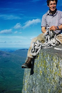 Young male climber sitting high up on a rock and holding a climbing rope, probably North Wales,