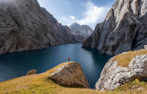 Tourist at the blue mountain lake between rocky steep mountain peaks, Kol Suu Lake, Kurumduk