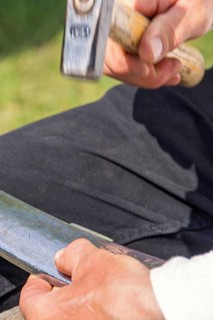 Man Peening a scythe blade using a hammer