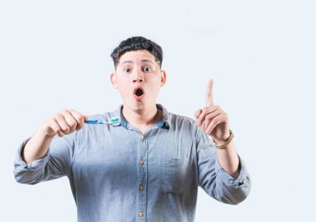 Surprised young man holding toothbrush pointing up isolated. Amazed man with toothbrush pointing up