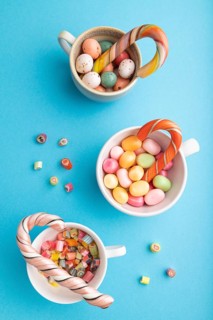 Heap of multicolored caramel candies in cups on blue pastel background. close up, top view, flat