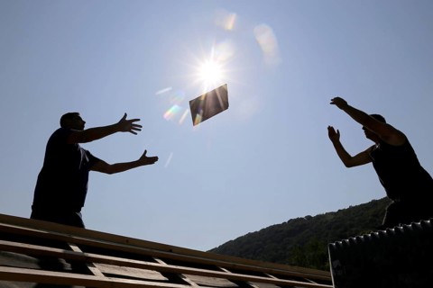 Silhouettes of two roofers throwing tiles at each other against the light