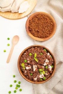 Quinoa porridge with green pea and chicken in wooden bowl on a white wooden background and linen