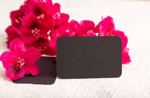 Black business card with purple azalea flowers on gray concrete background. side view, copy space,