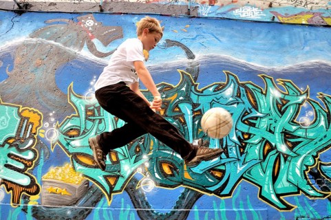 A ten-year-old boy plays with his football in front of a graffiti wall, football pitch in Germany