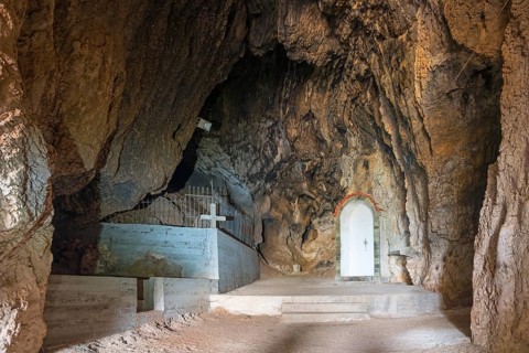 Interior view of a rocky cave with a tomb and a cross, a white niche visible, Church of Mary the