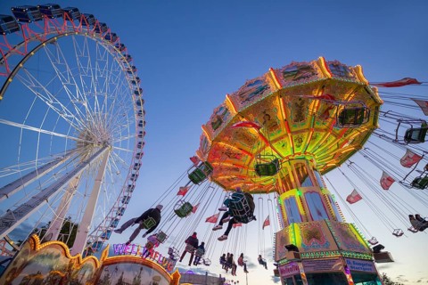A funfair at dusk with illuminated chain carousel and Ferris wheel, Europa Rad, rides, wave flight,
