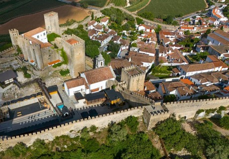 Aerial view of a historic city with a castle and surrounding city walls, embedded in a hilly and