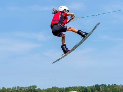 Boy or girl jumping with wakeboard, red life jacket, water sports, water skiing in wakepark