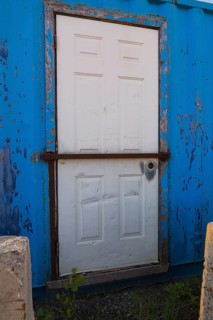 Blue painted metal building with white entrance door protected with steel bar, Quebec, Canada,