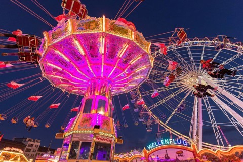 Illuminated carousel and Ferris wheel at night in a lively amusement park, funfair, wave flight,