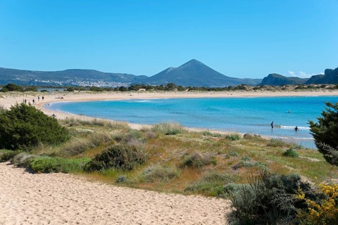 An idyllic beach with clear blue water and mountains in the background on a sunny day, Voidokilia