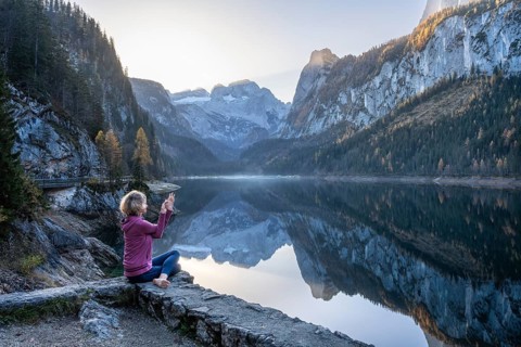 A woman doing yoga (Gomukhasana, Garudasana) by the lake. Vorderer Gosausee in autumn with a view