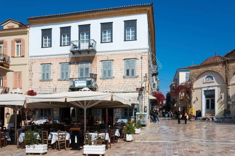 A square with a historic building, café with parasols and Mediterranean flair under a blue sky,