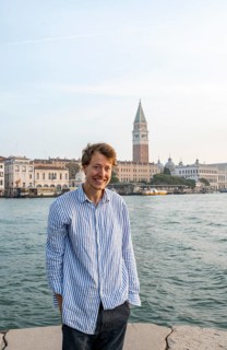 Young man in striped shirt and shorts on the banks of the Grand Canal, looking into the camera,