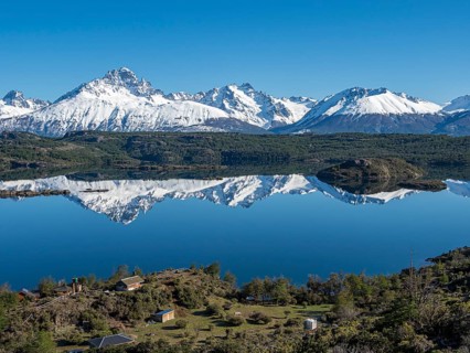The snow-covered Mt. Cerro Castillo is reflected in a lake, small farm by the lake, Patagonia,