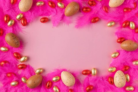 Frame made of eggs on pink feathers with red and gold chocolate eggs on a pink background