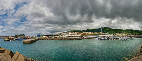 Coastal harbour with boats and houses surrounded by mountains under a cloudy sky, small town of