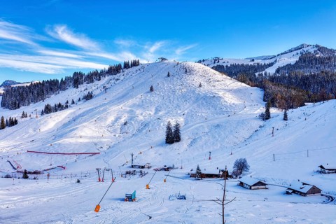 Snowy winter landscape with ski lift and huts against a clear blue sky, Sudelfeld