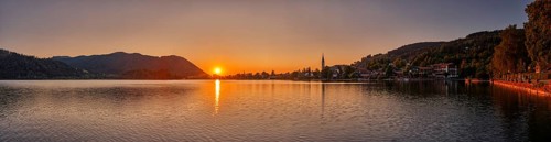 A peaceful sunset over a lake with mountains and a village in the background, Schliersee