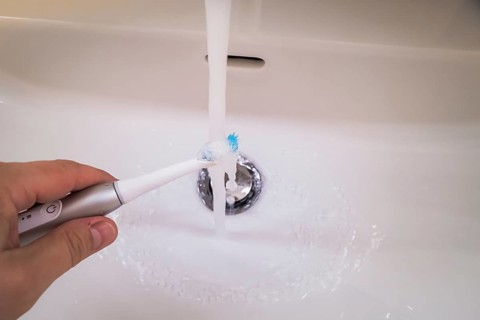 A bathroom tap is running while a toothbrush is held under the running water, symbolic image of