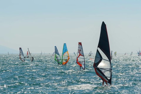 People windsurfing on a sunny day with clear blue skies and mountain backdrop, Lake garda, Torbole,