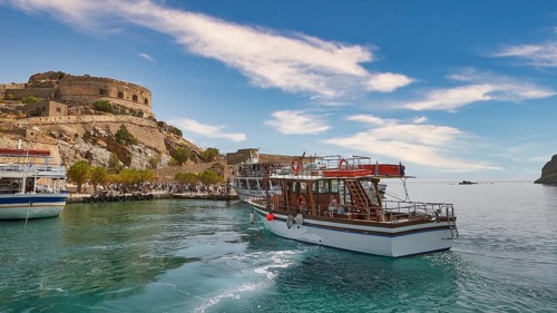 A white boat lies in a quiet harbour near a historic fortress under a blue sky, Venetian Sea