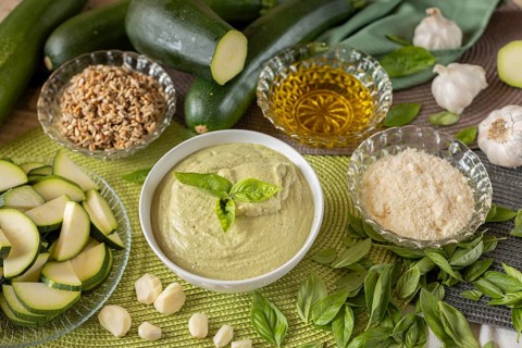 Bowl of courgette pesto surrounded by ingredients, courgettes, roasted sunflower seeds, parmesan,