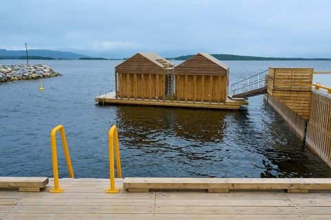 Outdoor sea pool by the fjord with small wooden sauna huts, overcast sky and calm water, Molde,