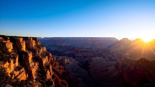 Sunrise over grand canyon in vibrant colors casting light on overhanging rock formations, AI