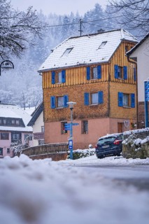 A yellow house with wooden panelling and blue shutters in the snow, Enzklösterle, Calw district,
