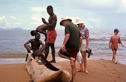 Tourists with local young men looking at a dugout tree on the beach of Lake Malawi, Malawi,