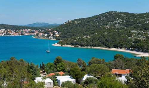 Coastal town with pine trees and sailing boats, surrounded by blue sea, bay near Tisno,